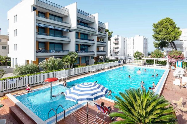 Piscina all'aperto con ombrelloni e palazzi bianchi.