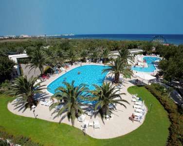 Piscina circondata da palme e lettini, con il mare sullo sfondo.