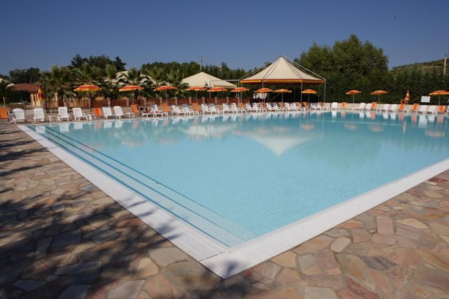 Grande piscina all'aperto con lettini e ombrelloni arancioni.