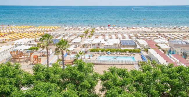 Vista sulla spiaggia con ombrelloni gialli e piscina.