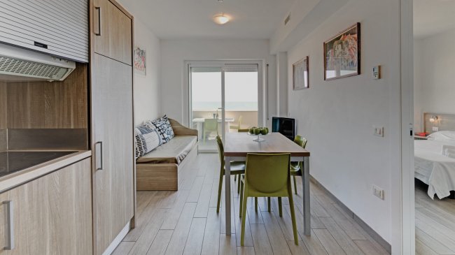 Sala da pranzo luminosa con tavolo, sedie e vista balcone.