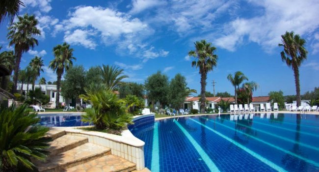 Piscina all'aperto con palme e cielo azzurro.