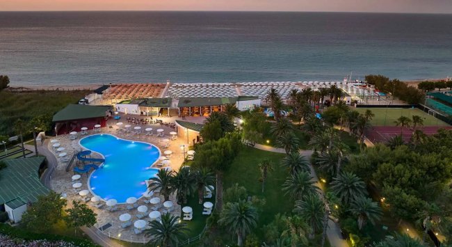 Resort con piscina e giardino vicino al mare al tramonto.