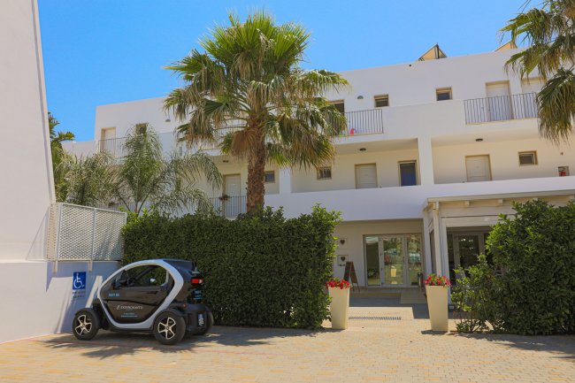 Edificio bianco con palme e un'auto elettrica parcheggiata.