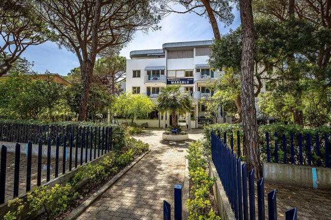 Edificio bianco circondato da alberi e siepi.
