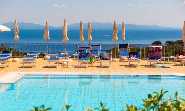 Piscina con sdraio blu e ombrelloni vista mare.