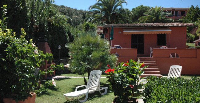 Giardino con sedie a sdraio e una casa arancione sullo sfondo.