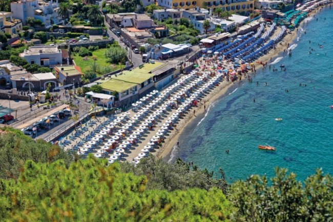 Spiaggia affollata con ombrelloni bianchi.