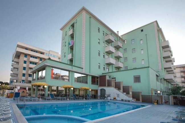 Edificio verde con piscina e lettini.