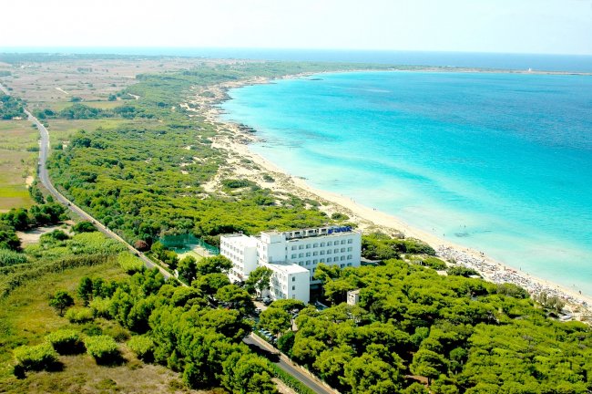 Hotel circondato da vegetazione vicino a una spiaggia con mare turchese.