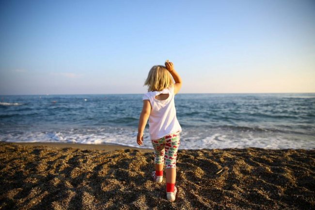 Bambina cammina verso il mare sulla spiaggia.