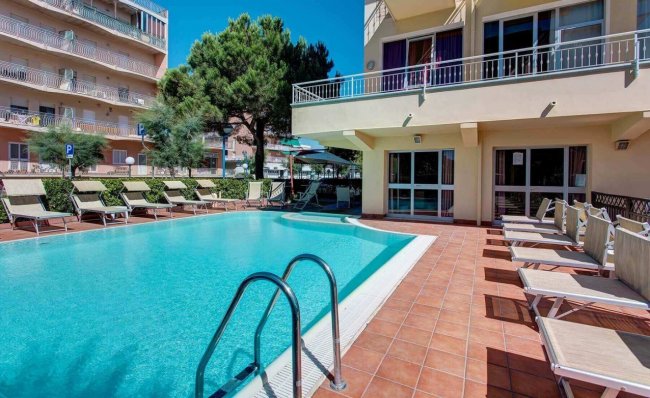 Piscina all'aperto con sdraio e edificio sullo sfondo.