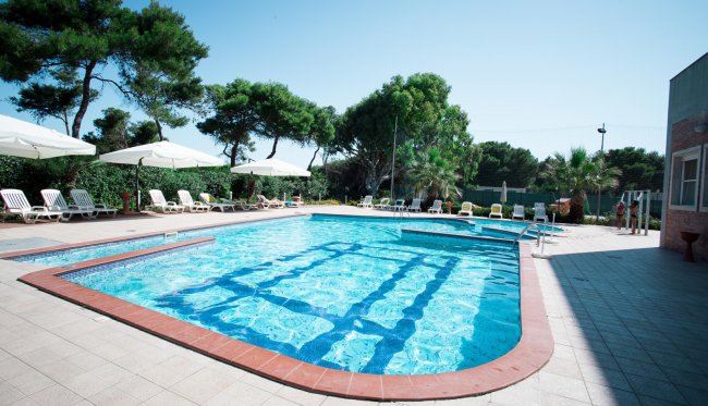 Piscina all'aperto circondata da lettini e ombrelloni.