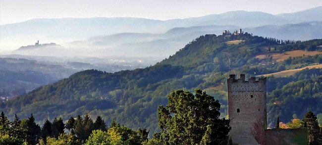 Colline verdi e torre medievale in una giornata leggermente nebbiosa.