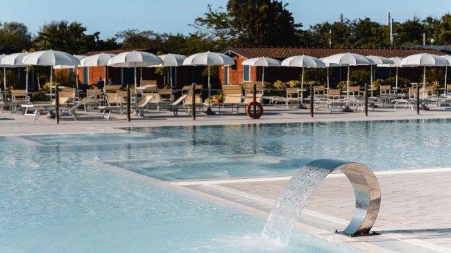 Piscina con getto d'acqua e ombrelloni bianchi.