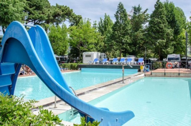 Piscina con uno scivolo blu, lettini in fondo.