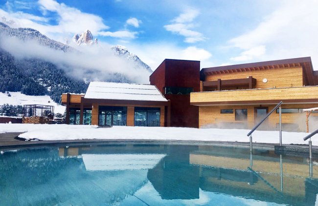 Piscina all'aperto con vista su montagne innevate e cielo nuvoloso.