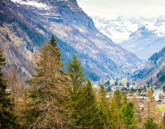 Valle con montagne, alberi e villaggio al fondo.