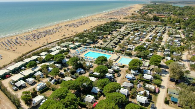 Panoramica di un campeggio con spiaggia affollata e piscine.